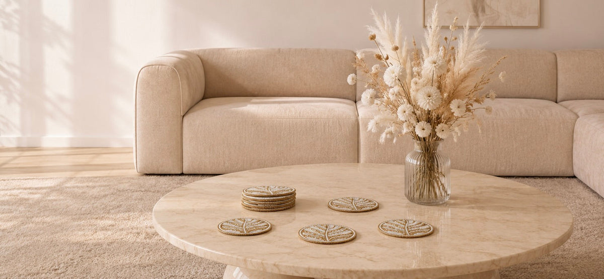 Luxe handgemaakte kralen onderzetters van My Marble op een marmeren salontafel met beige woonaccessoires en witte bloemen.