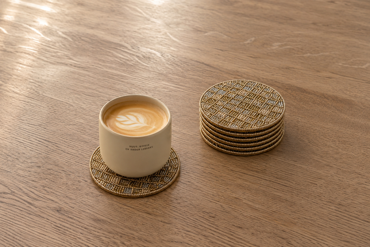 Koffiekopje op een handgemaakte kralen onderzetter van My Marble met een stapel luxe onderzetters op een houten koffietafel.