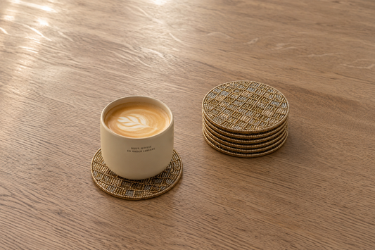 Koffiekopje op een handgemaakte kralen onderzetter van My Marble met een stapel luxe onderzetters op een houten koffietafel.